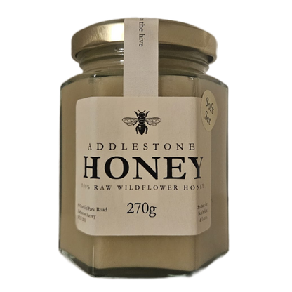 A jar of Adlestone Honey Raw Wildflower Honey, 270g, with a gold lid and a cream-colored label featuring a bee logo.